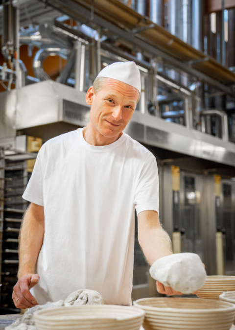 Bäcker Müller, Bild mit Bäcker der ein Brot-Teig in der Hand hält
