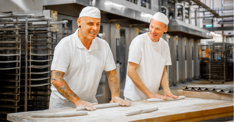 Bäcker Müller, Bild mit zwei Bäcker die lachen und gerade den Teig rollen auf einem mit Mehl bestreute Arbeitsfläche